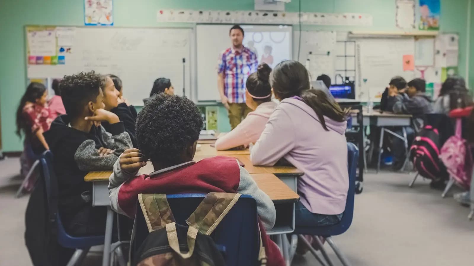 Students in a classroom facing a teacher at a whiteboard