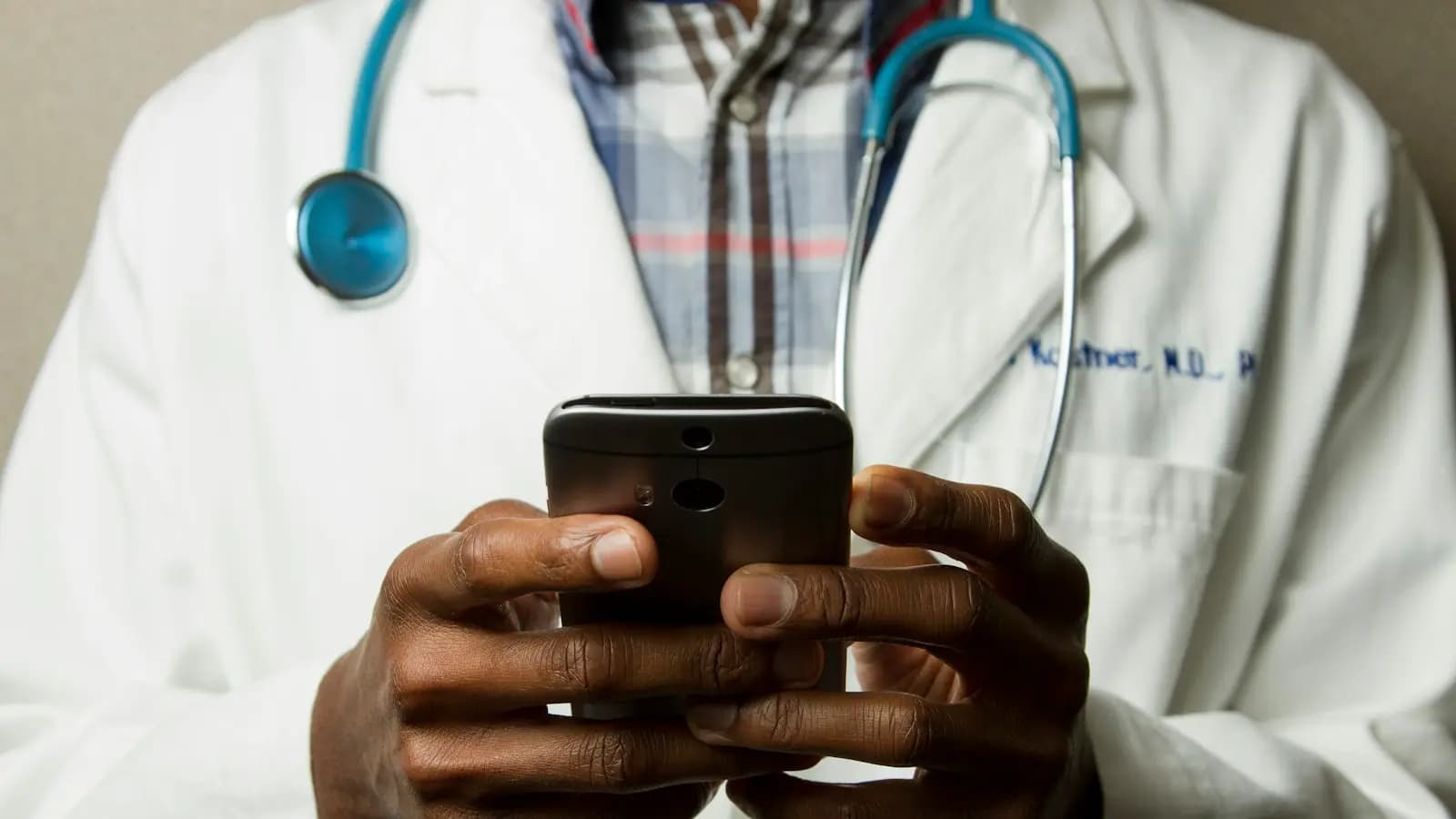 Clinician in a white coat with a stethoscope using a mobile device