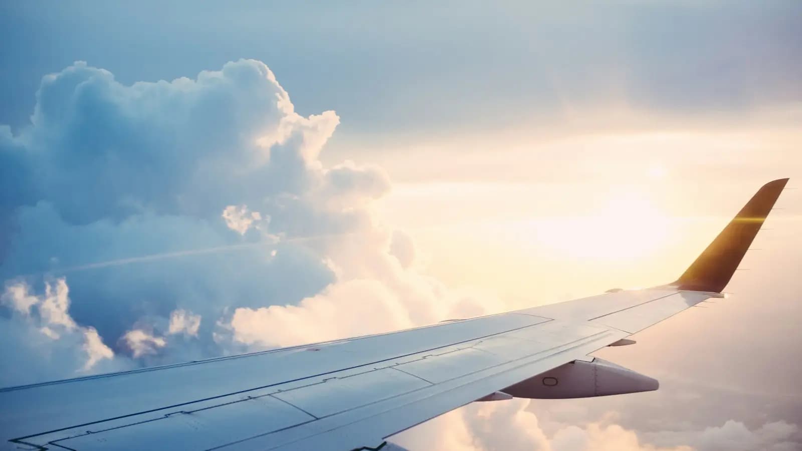 Airplane wing above sunlit clouds